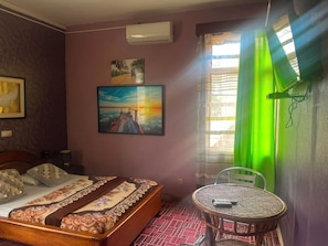 Ein Schlafzimmer mit Bett, einem Bild, einem Fenster mit Vorhängen und einem kleinen Tisch.