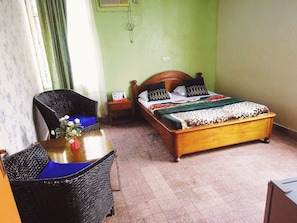 Ein Schlafzimmer mit einem Bett, einem Nachttisch, einem Korbstuhl und einem Tisch mit einer Vase.