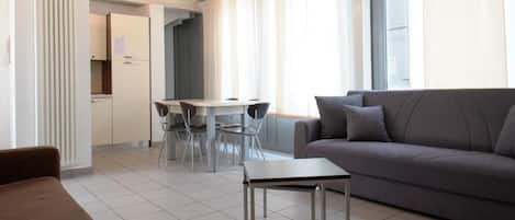 A modern living room with a sofa, a small table, and a dining area with chairs.