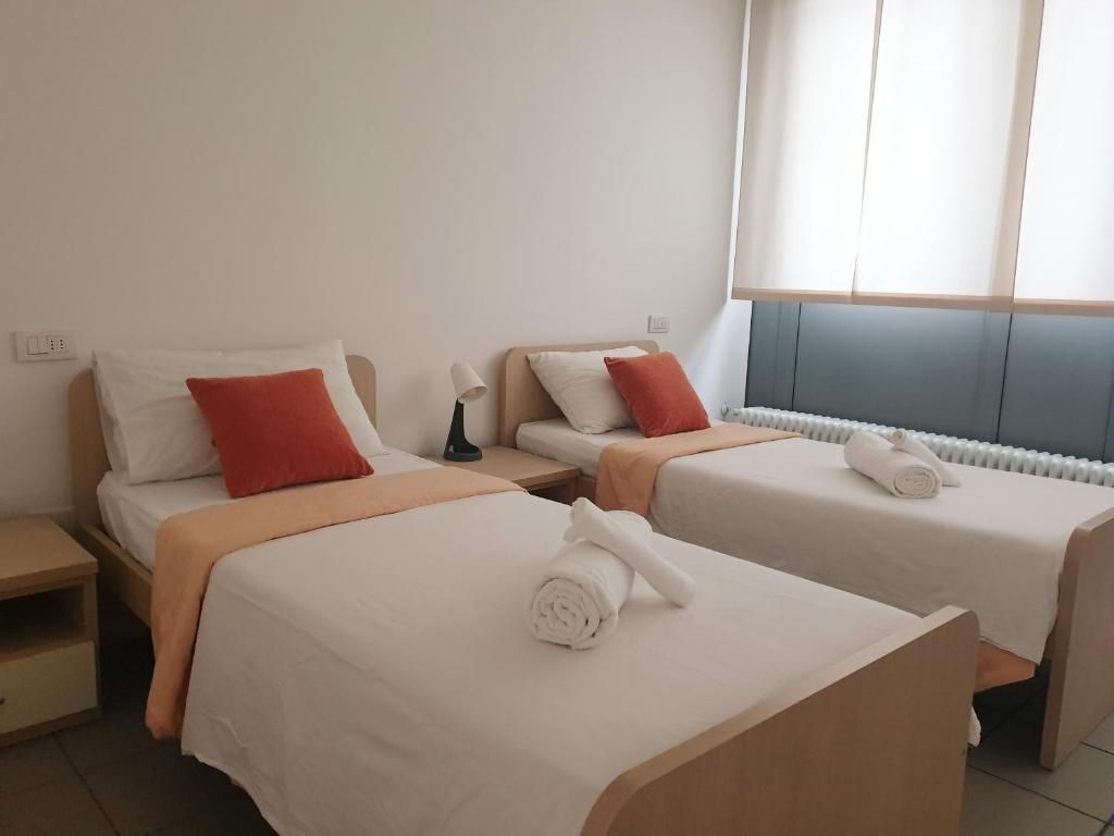Een hotelkamer met twee bedden, elk voorzien van een kussen en een opgerolde handdoek.