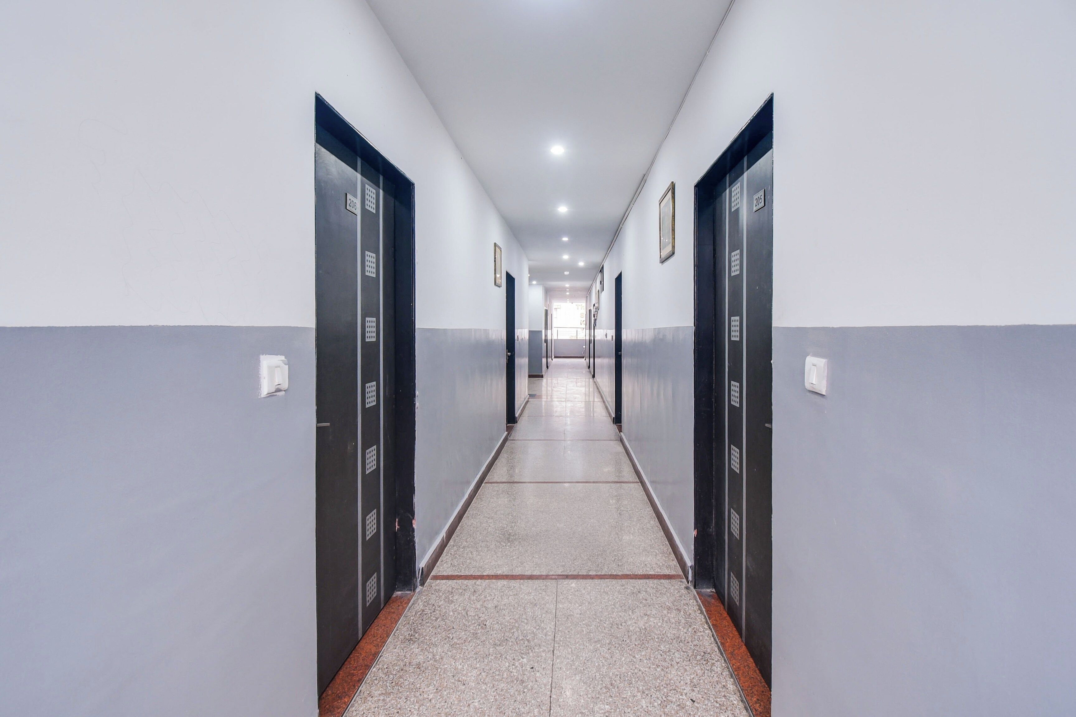 A long, narrow hallway with doors on both sides, leading to a bright room at the end.