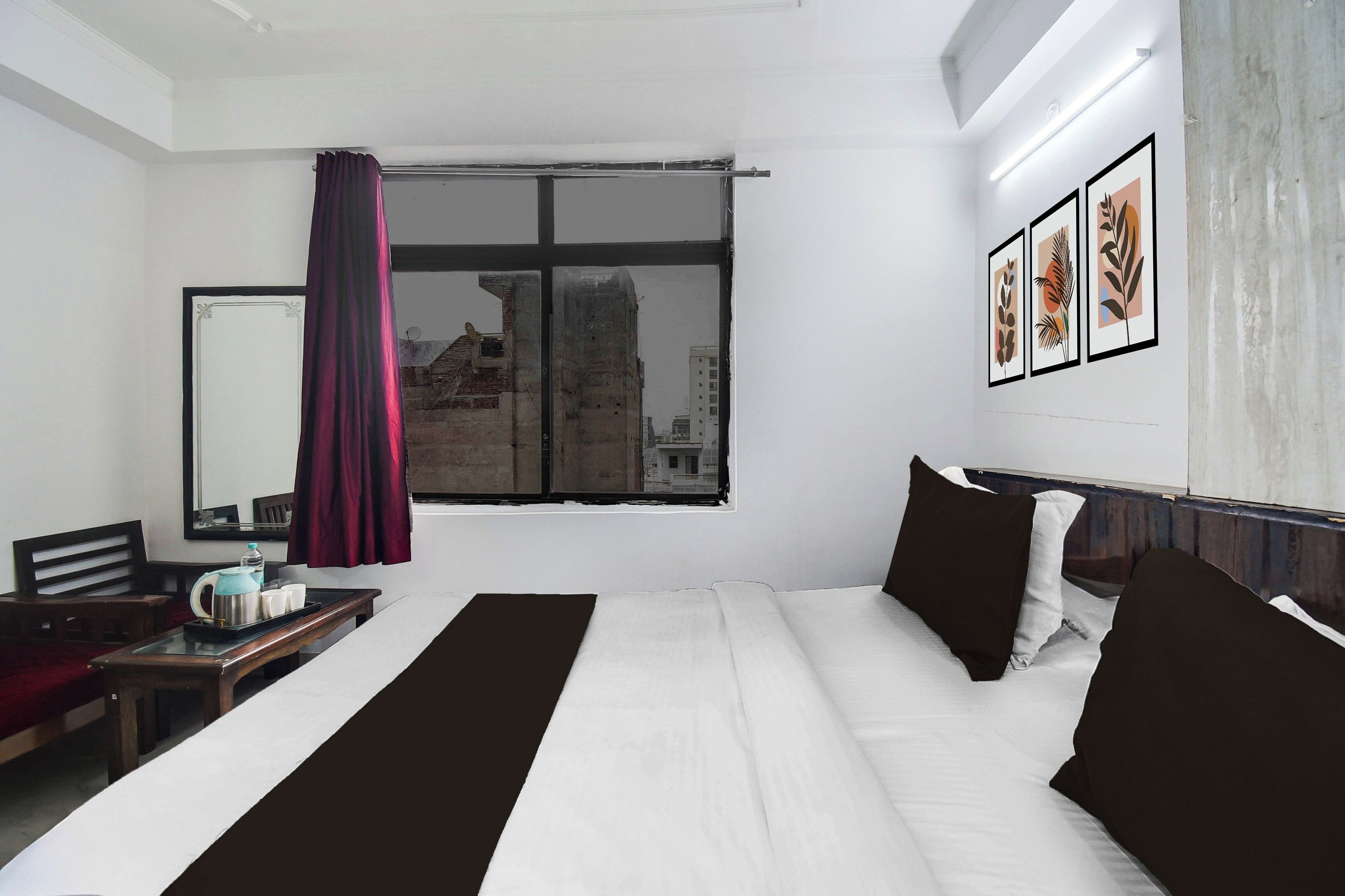 Habitación de hotel con una cama grande, un escritorio con hervidor y tazas, una ventana con vistas a edificios y cuadros en la pared.