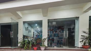 Entrada de un edificio con puertas de cristal, plantas en macetas y una escalera que sube.