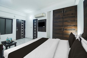 Una habitació d'hotel amb un llit gran, un armari, una taula de treball amb una cadira i una finestra.