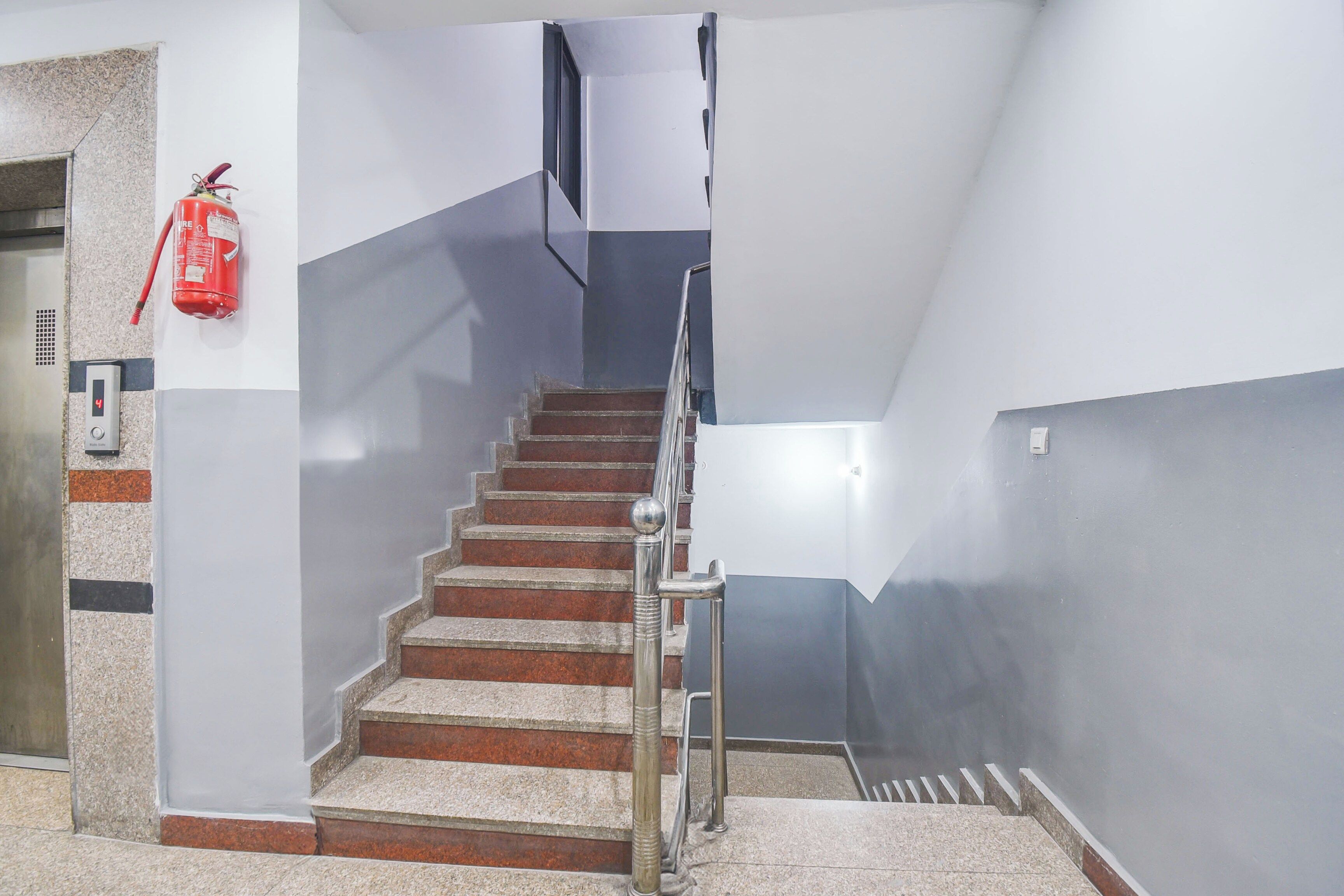 A staircase with a handrail, a fire extinguisher mounted on the wall, and a digital display on the wall.