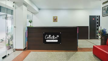 Una recepción con un cartel que indica servicio de la empresa. Hay un cuadro en la pared, una planta en maceta y una silla roja.