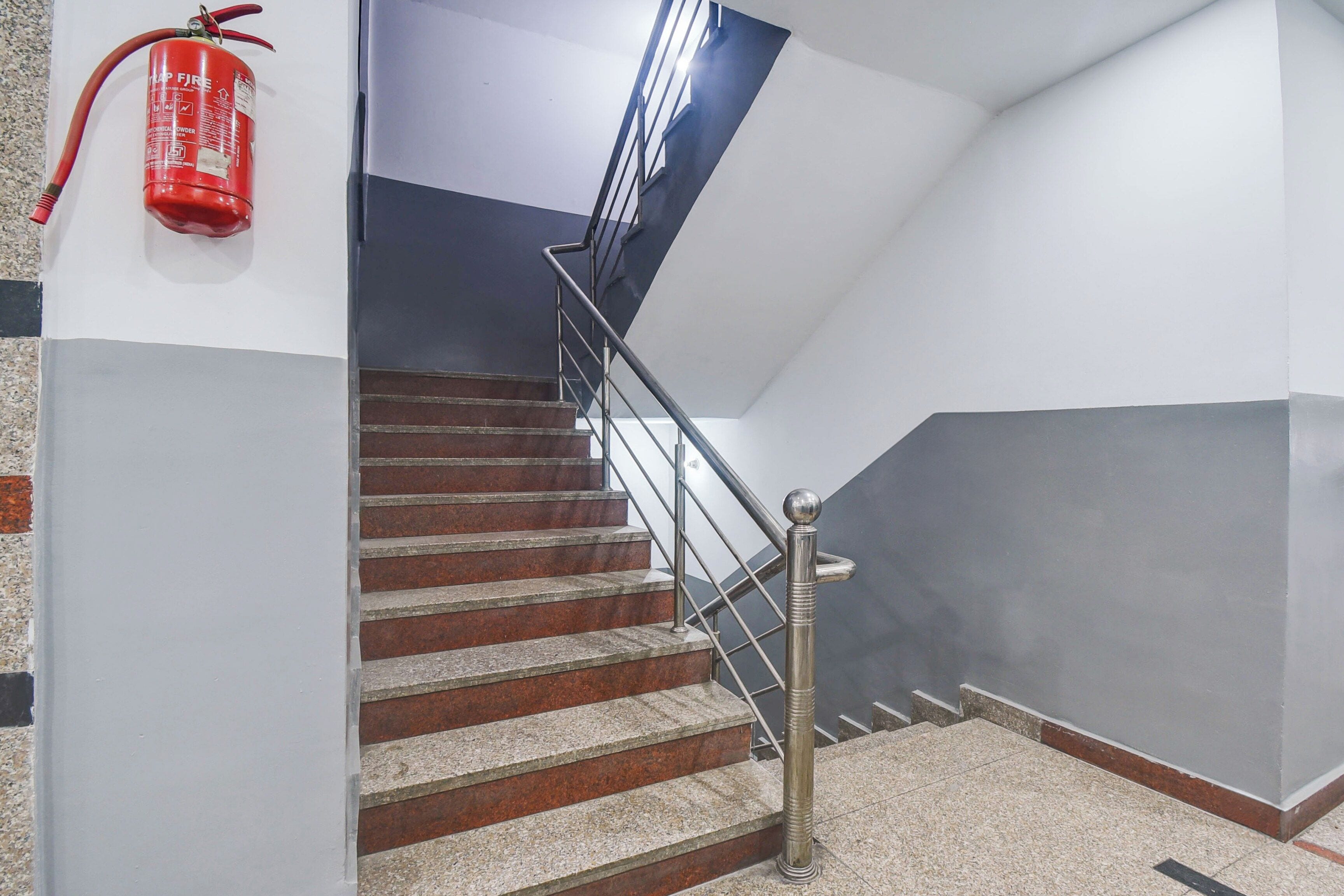 Un escalier avec une rampe métallique, un extincteur fixé au mur et une lance d’incendie sur le côté gauche.