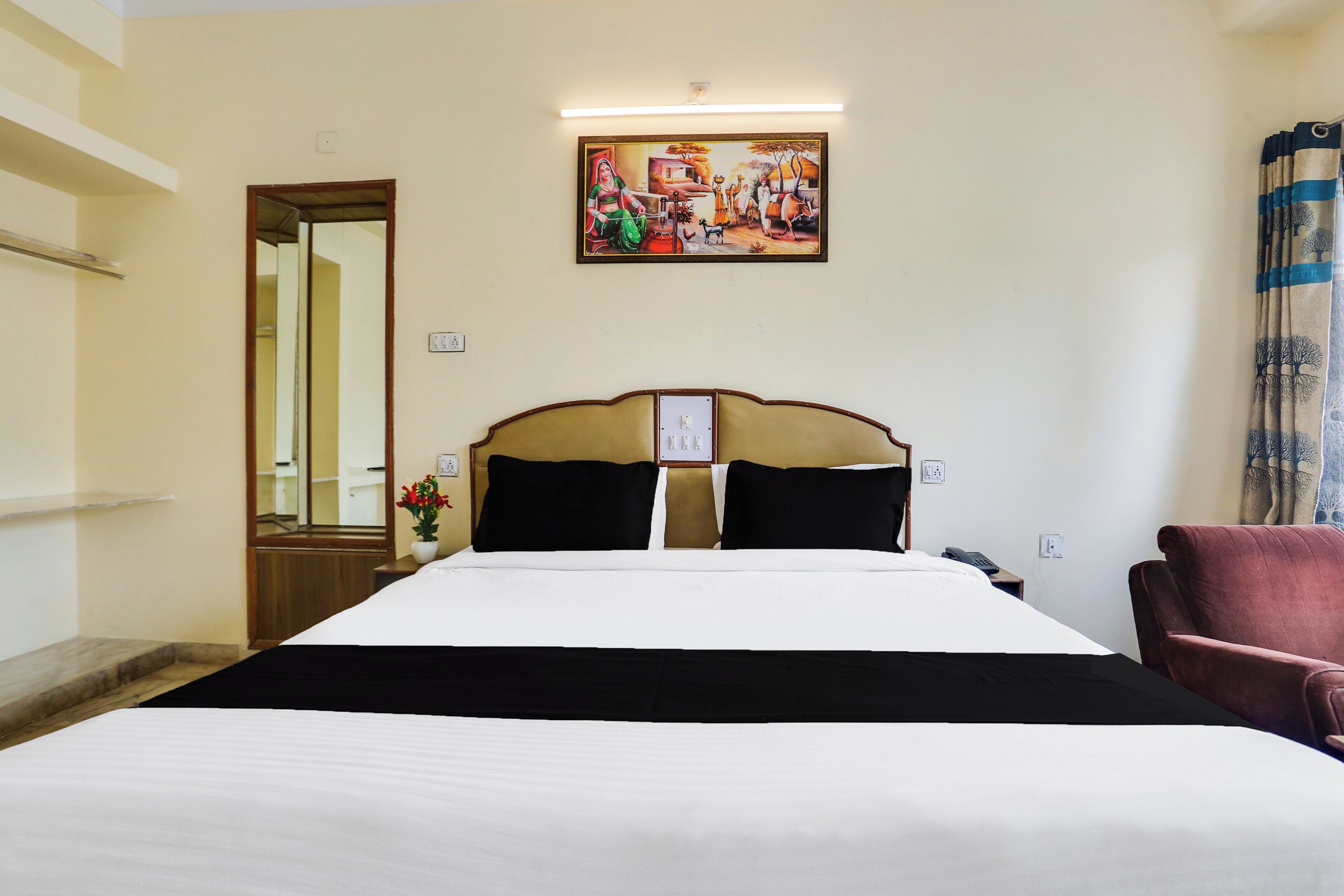 A hotel room with a bed, a chair, a painting on the wall, and a door.