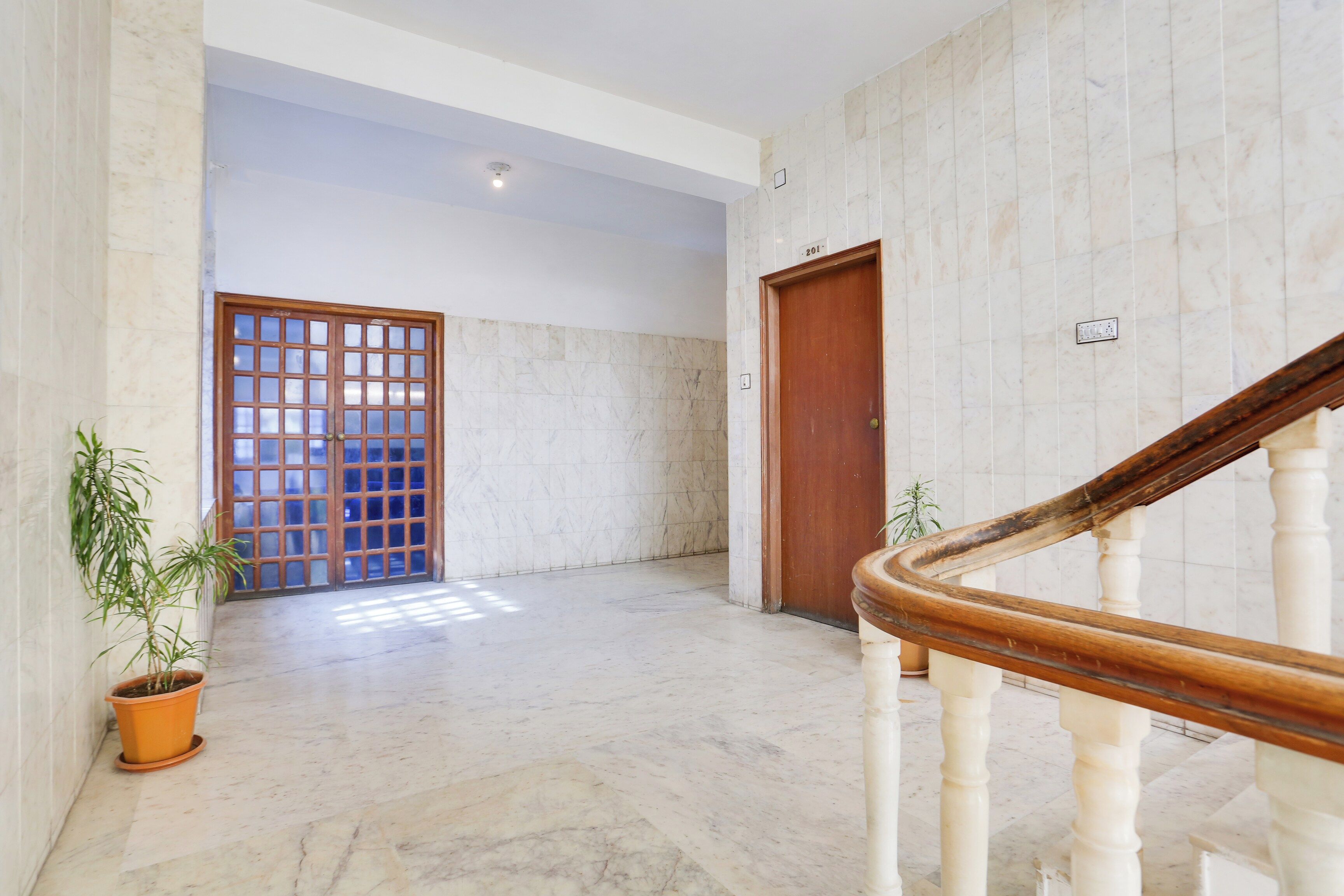 A hallway with a marble floor, a wooden door, and a staircase with a wooden handrail.