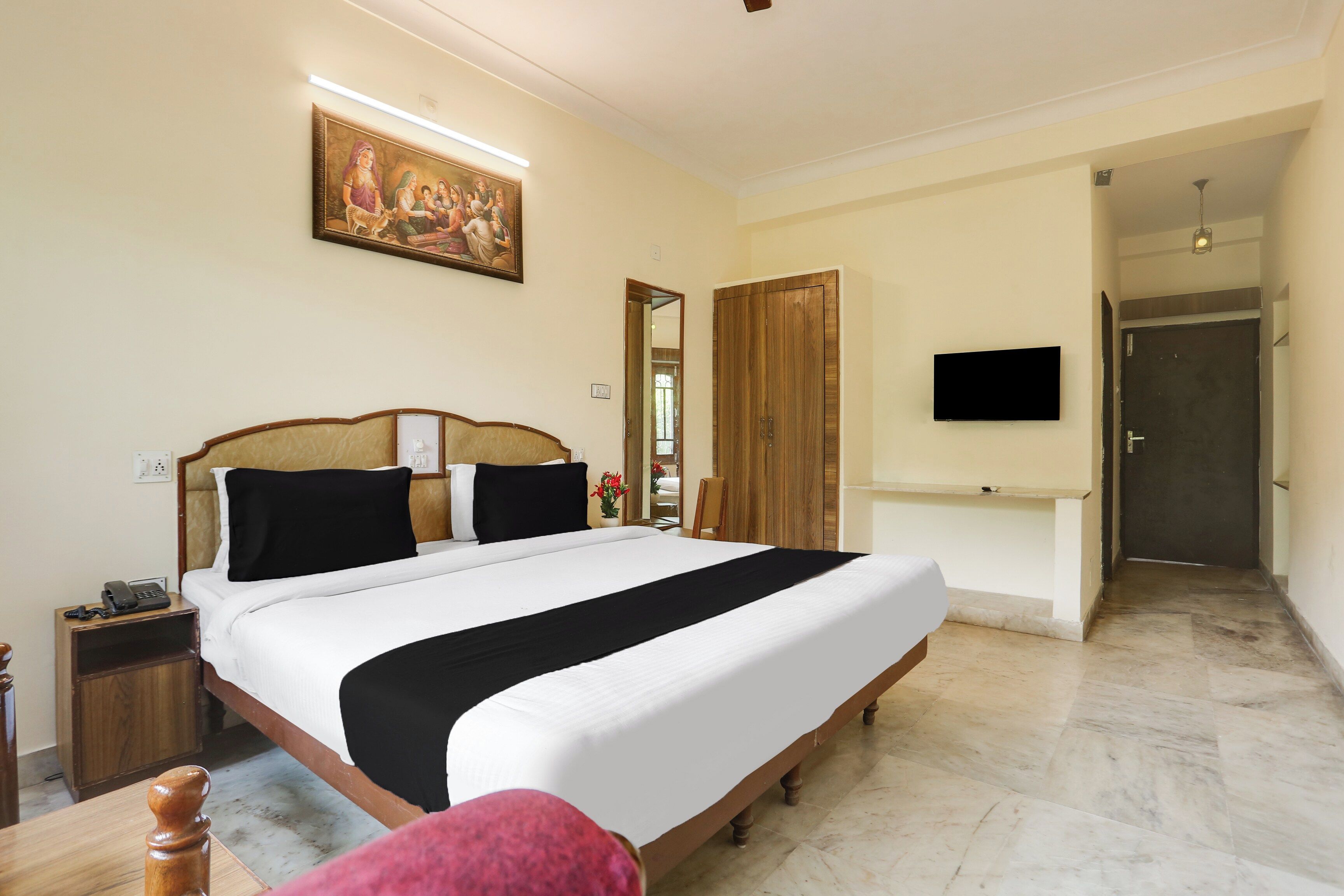 A hotel room with a large bed, a bedside table with a phone, a flat-screen TV mounted on the wall, and a wooden wardrobe.