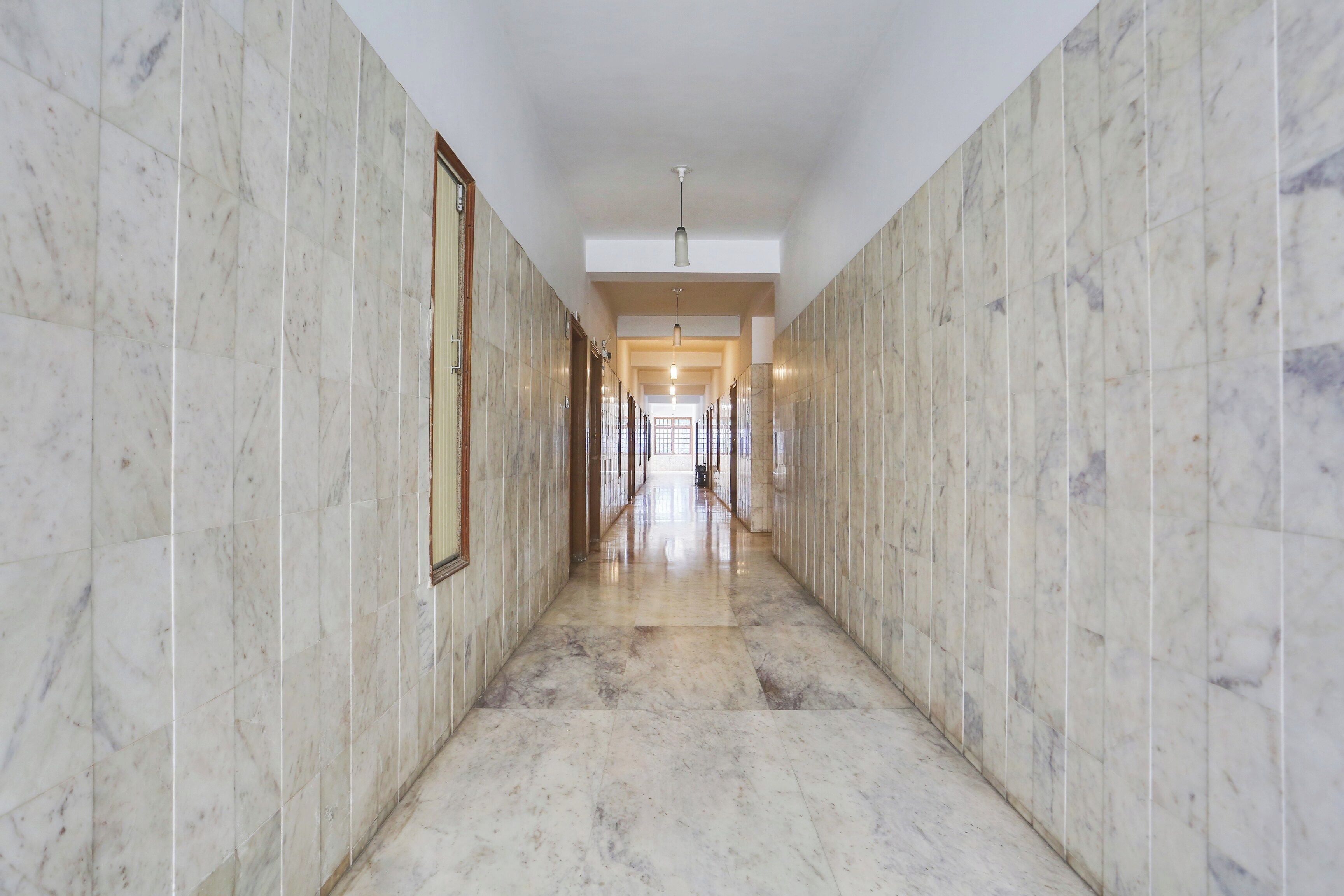 A corridor with marble walls and a polished floor, leading to a door at the end.