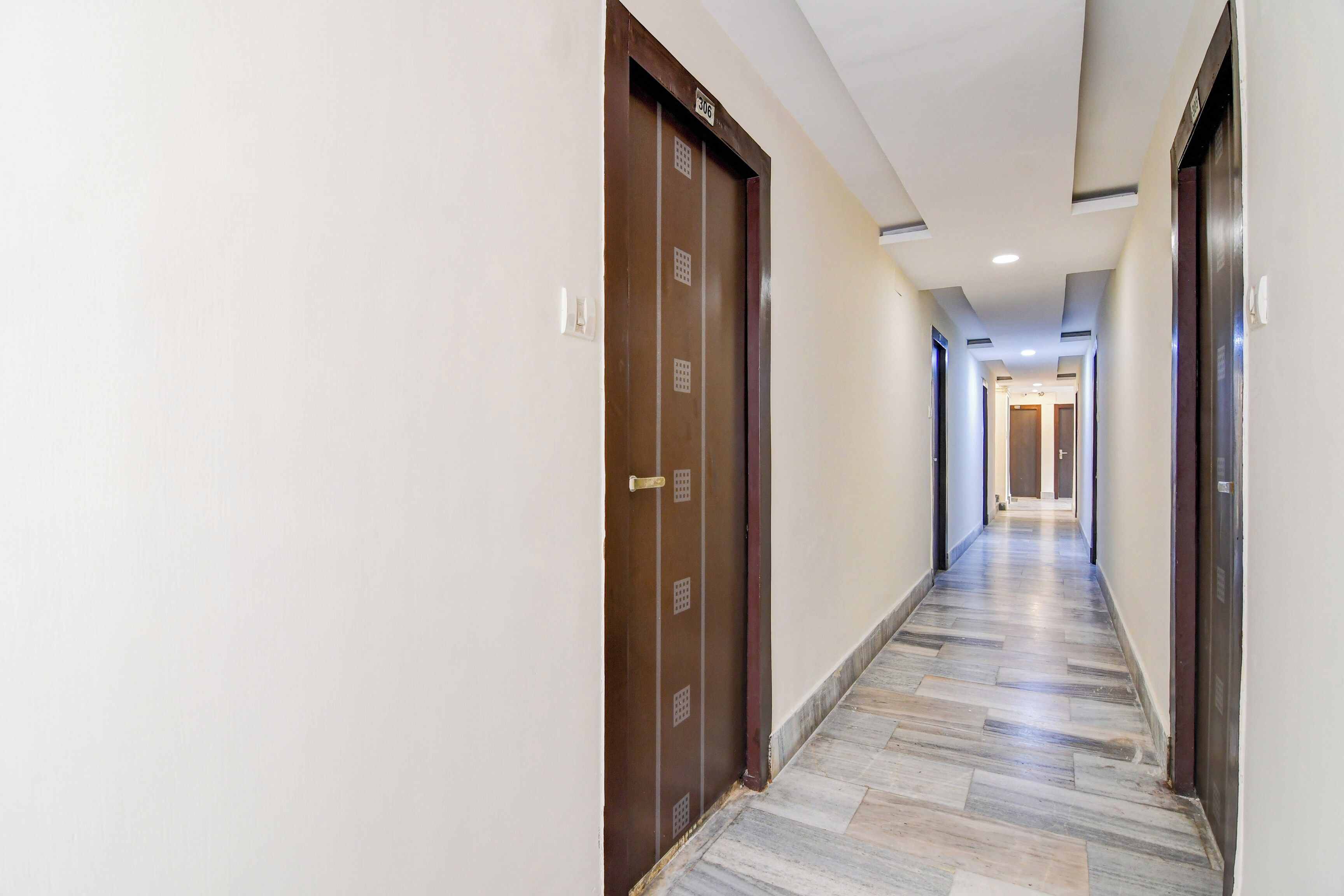 A hotel hallway with a marble floor, wooden doors, and a ceiling with recessed lighting.