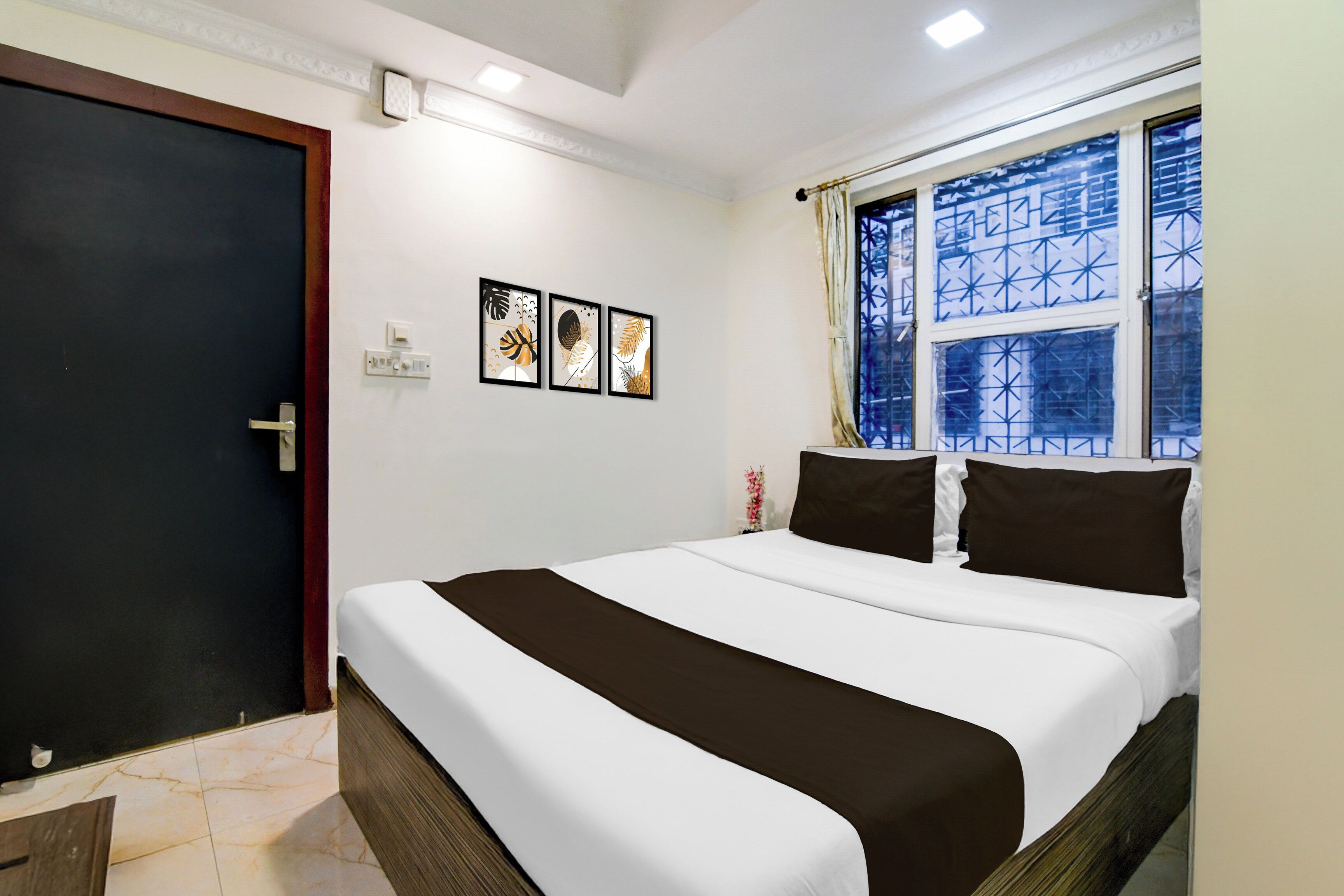 A hotel room with a bed, a door, a window with a view, and wall-mounted artwork.
