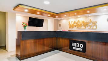 Un mostrador de recepción de hotel con un televisor de pantalla plana, un jarrón de flores y un letrero que indica que el hotel cuenta con servicios para empresas.