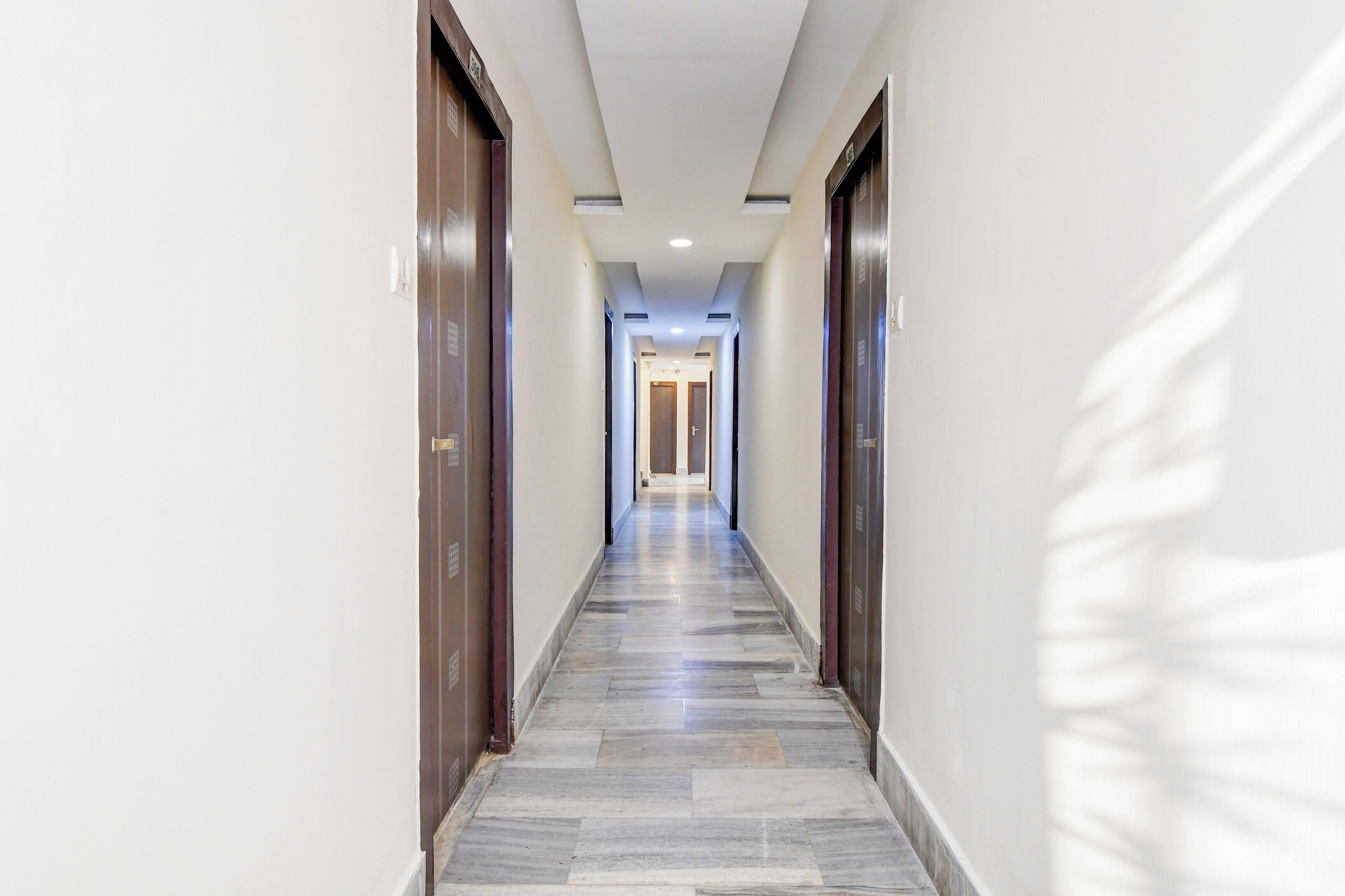 Pasillo de hotel con piso de baldosas, puertas de madera e iluminación empotrada en el techo.