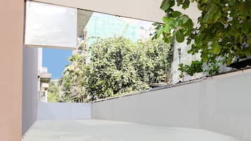 A narrow outdoor corridor with a concrete wall on one side and a building with a balcony on the other.
