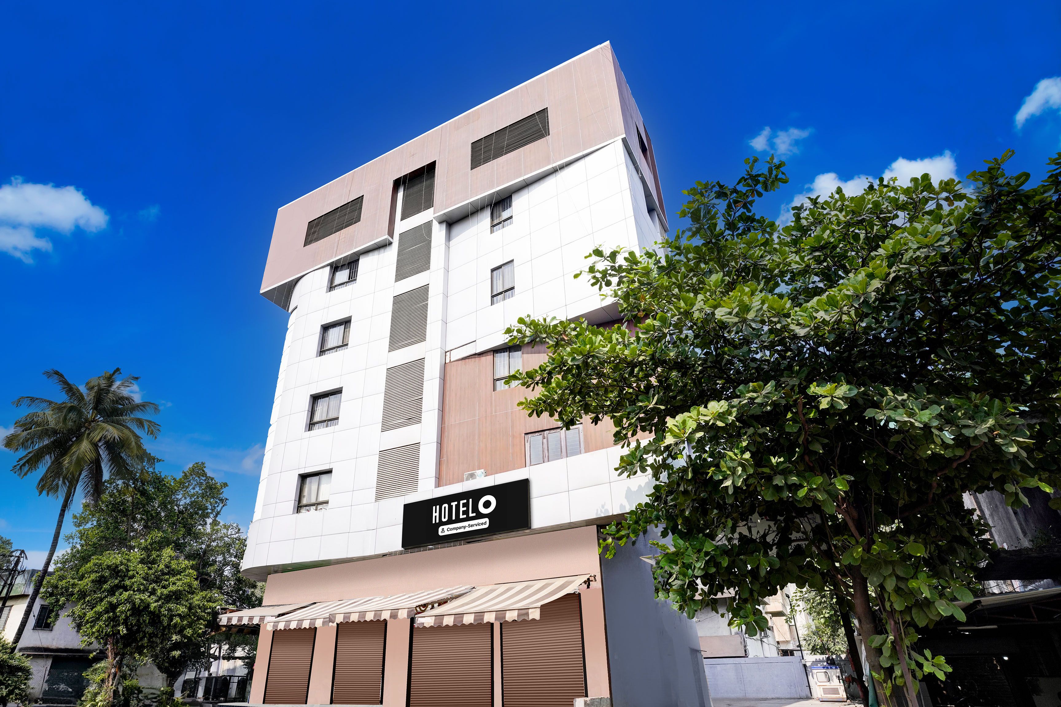 A multi-story hotel with a modern facade, a sign indicating it is company-serviced, and a covered entrance with awnings.