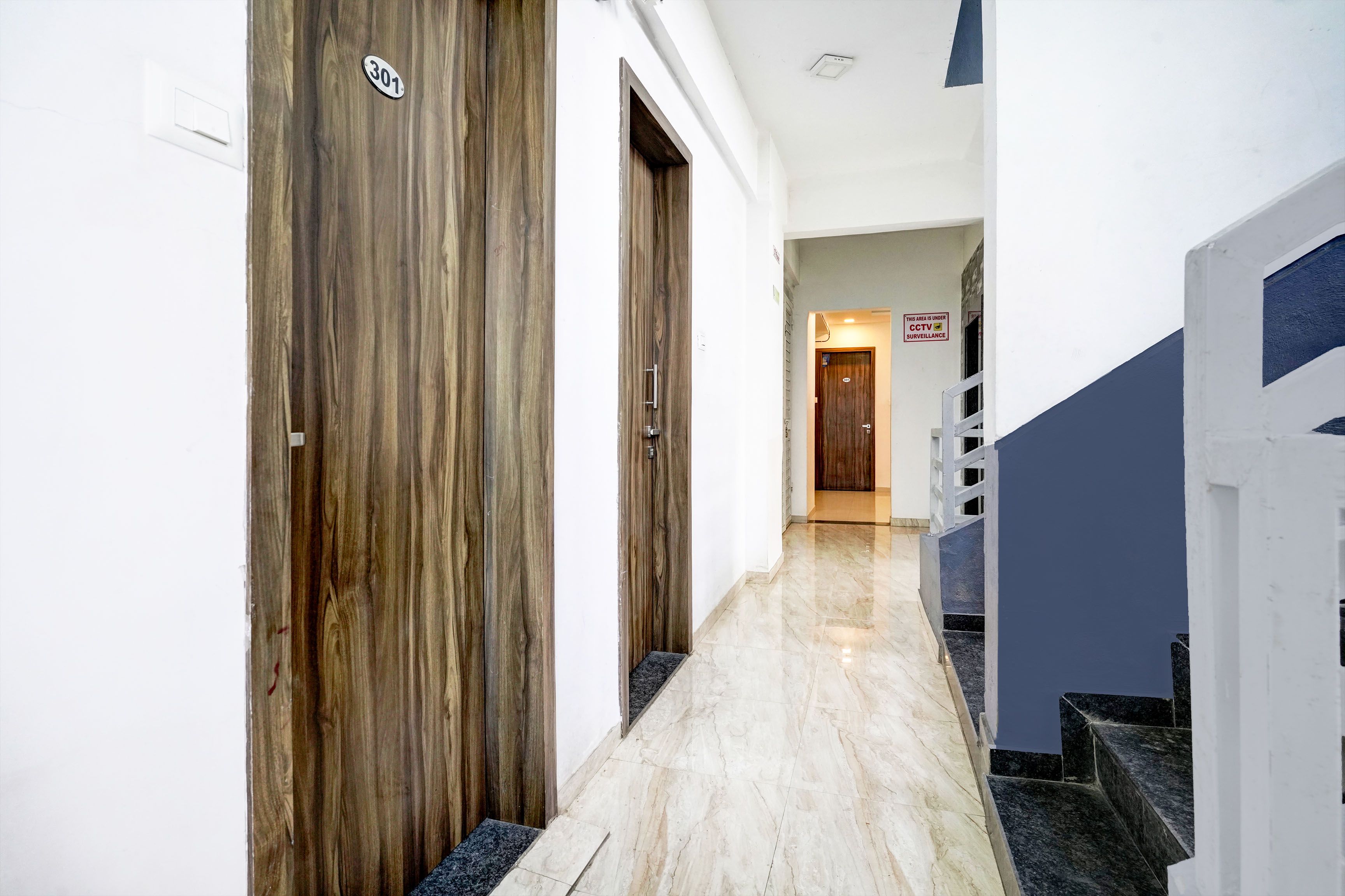 A hallway with wooden doors, a tiled floor, and a staircase with a blue accent.