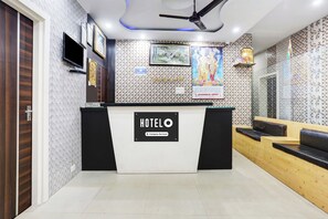 Zona de recepción de un hotel, con mostrador de recepción, un televisor y una pared decorada con carteles religiosos.
