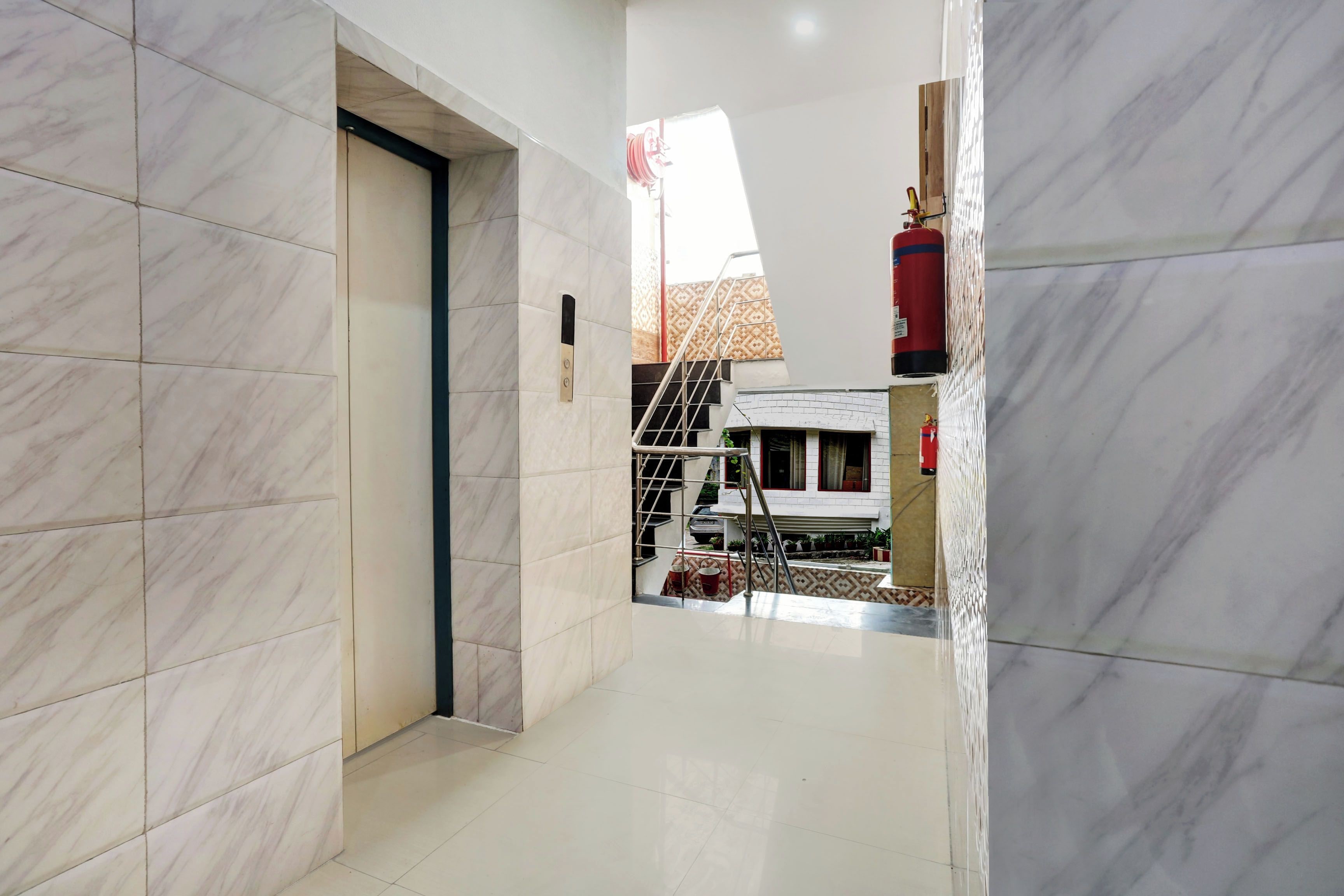 A hallway with marble flooring, a door, and a staircase leading to a building with a patterned facade.