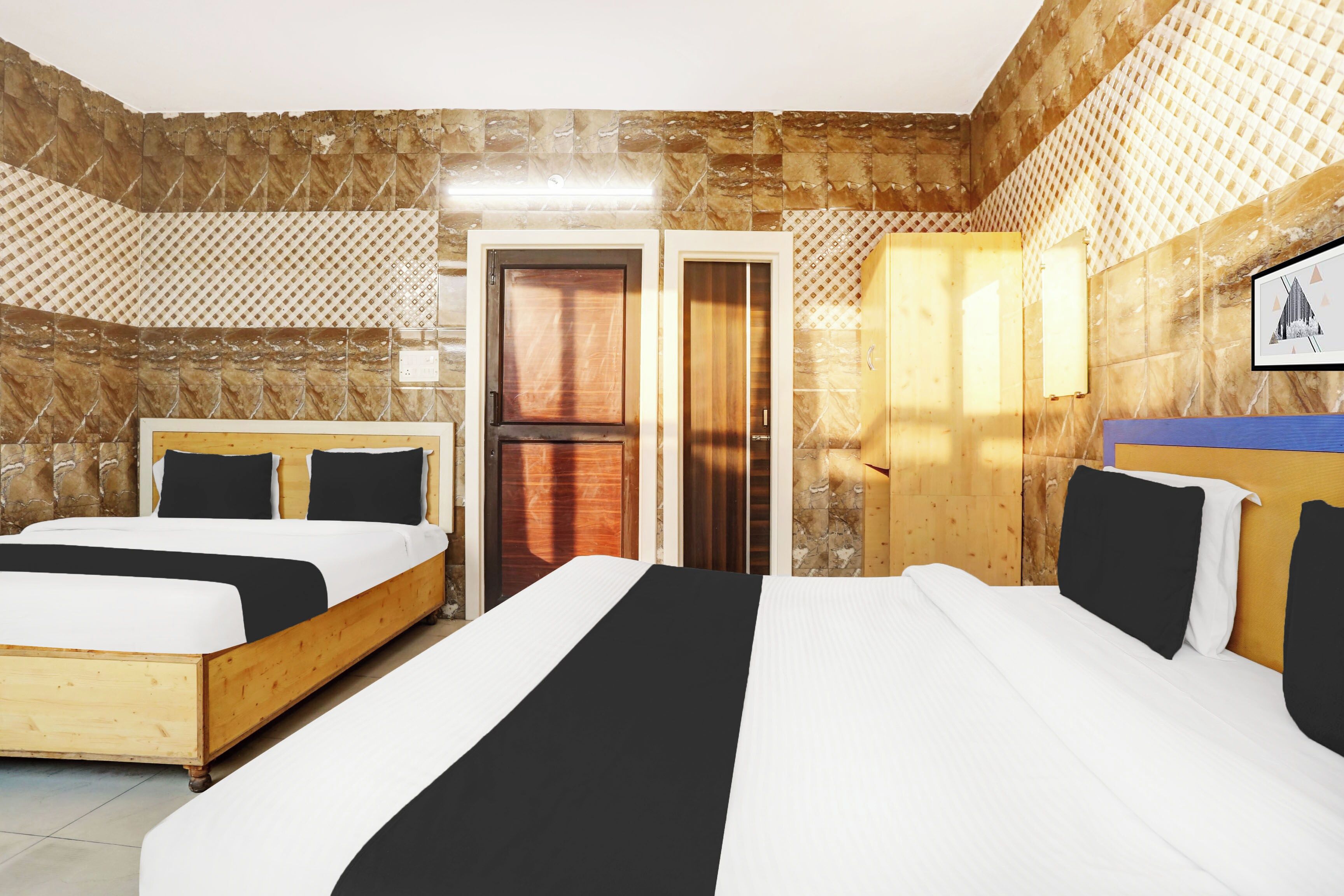 A hotel room with two beds, a wooden wardrobe, a door, and a wall-mounted light fixture.
