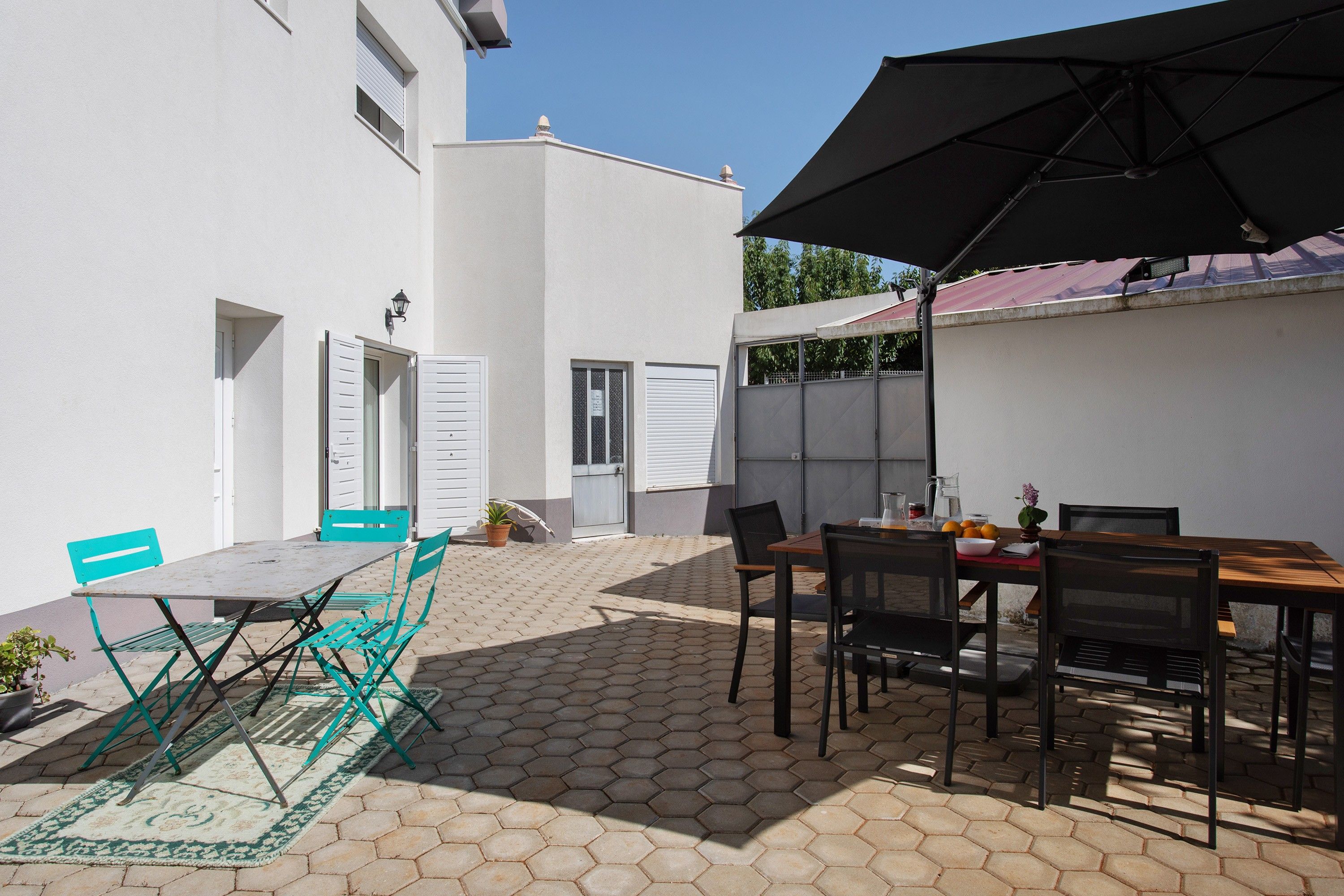En udendørs terrasse med et bord, stole, en potteplante og en stor parasol.