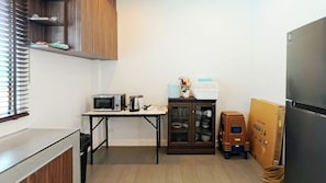 Eine kompakte Küche mit Mikrowelle, einer Vitrine, einem Kühlschrank und einem Tisch mit Küchenutensilien.