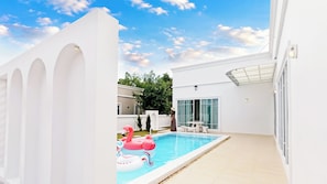 Ein Swimmingpool mit Schwimmreifen in Form von Flamingos, eine überdachte Terrasse und ein weißes Gebäude mit Rundbogenfenstern.