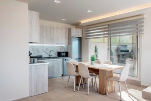 A modern kitchen with a marble backsplash, a built-in oven, and a dining area with a wooden table and chairs. - Magic View Apartment (Zakynthos)