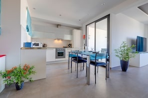 Eine moderne Küche mit weißen Schränken, ein Essbereich mit blauen Stühlen und ein großes Fenster.