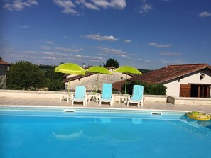 A swimming pool with lounge chairs and umbrellas, a building with a tiled roof, and a clear sky. - Holiday Home 'Les Deux Indeaux' with Wi-Fi (Lusignac)