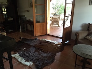 A room with a large fur rug, a wooden door leading outside, and a dining area visible through the door. - Holiday Home 'Les Deux Indeaux' with Wi-Fi (Lusignac)