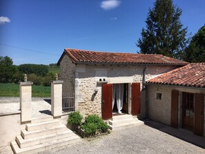A small stone building with a tiled roof, a set of steps leading to the entrance, and a small garden area. - Holiday Home 'Les Deux Indeaux' with Wi-Fi (Lusignac)
