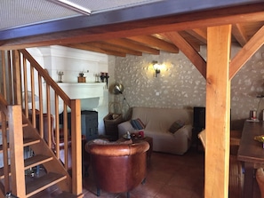 Un salon chaleureux avec un escalier en bois, une cheminée, un canapé et un coin repas.
