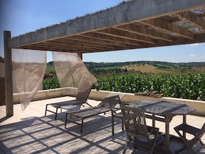 An outdoor patio with a pergola, a table, chairs, and a view of a cornfield. - Holiday Home 'Les Deux Indeaux' with Wi-Fi (Lusignac)