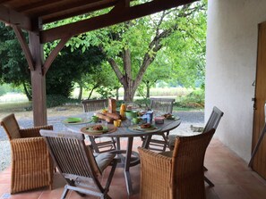 Eine Terrasse im Freien mit einem runden Esstisch, umgeben von Korbstühlen, und einer Holzhütte darüber.