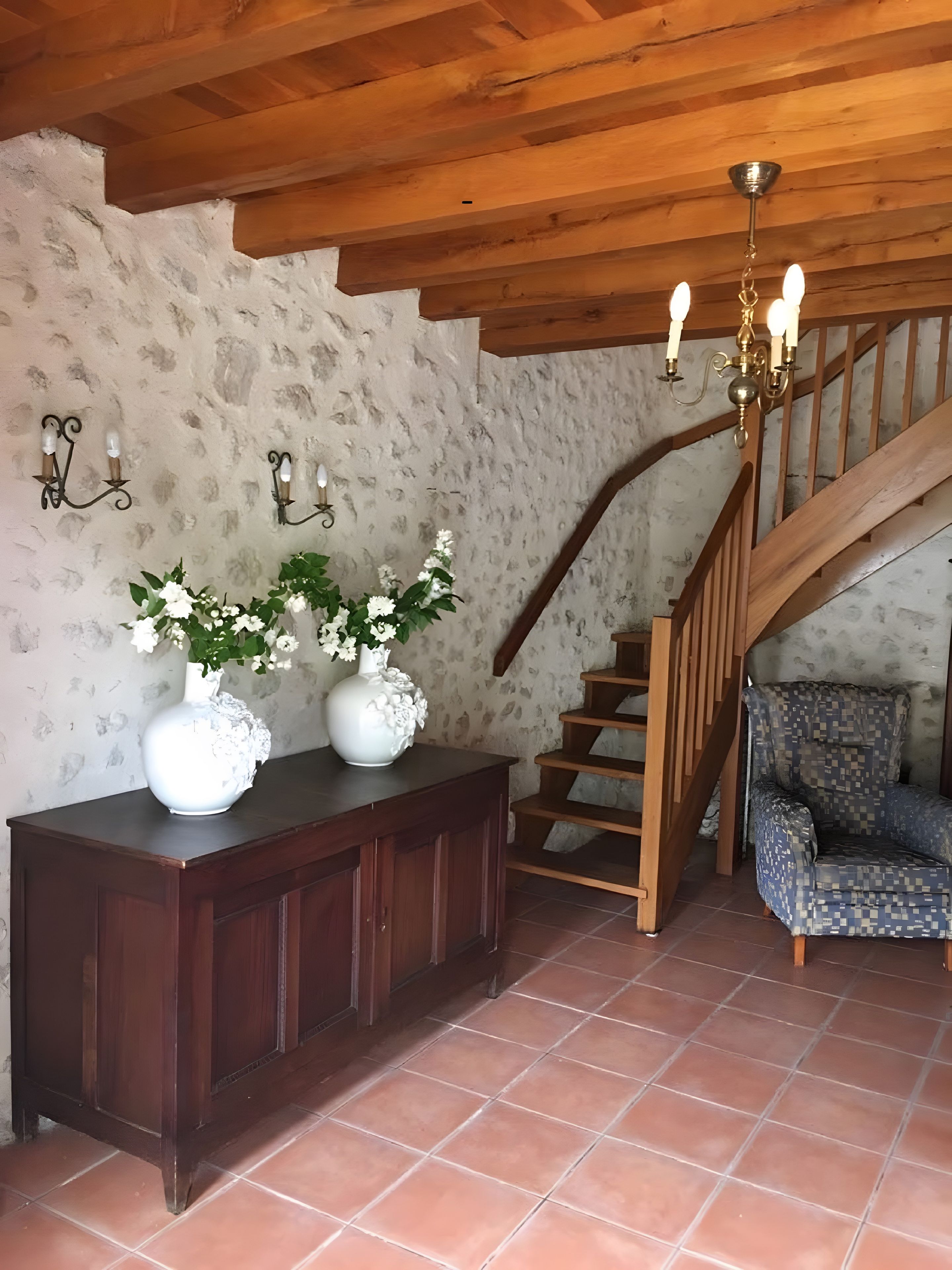 Ein rustikales Interieur mit einer Holztreppe, einem dunklen Holzkonsolentisch und weißen Vasen sowie einem gemusterten Sessel.