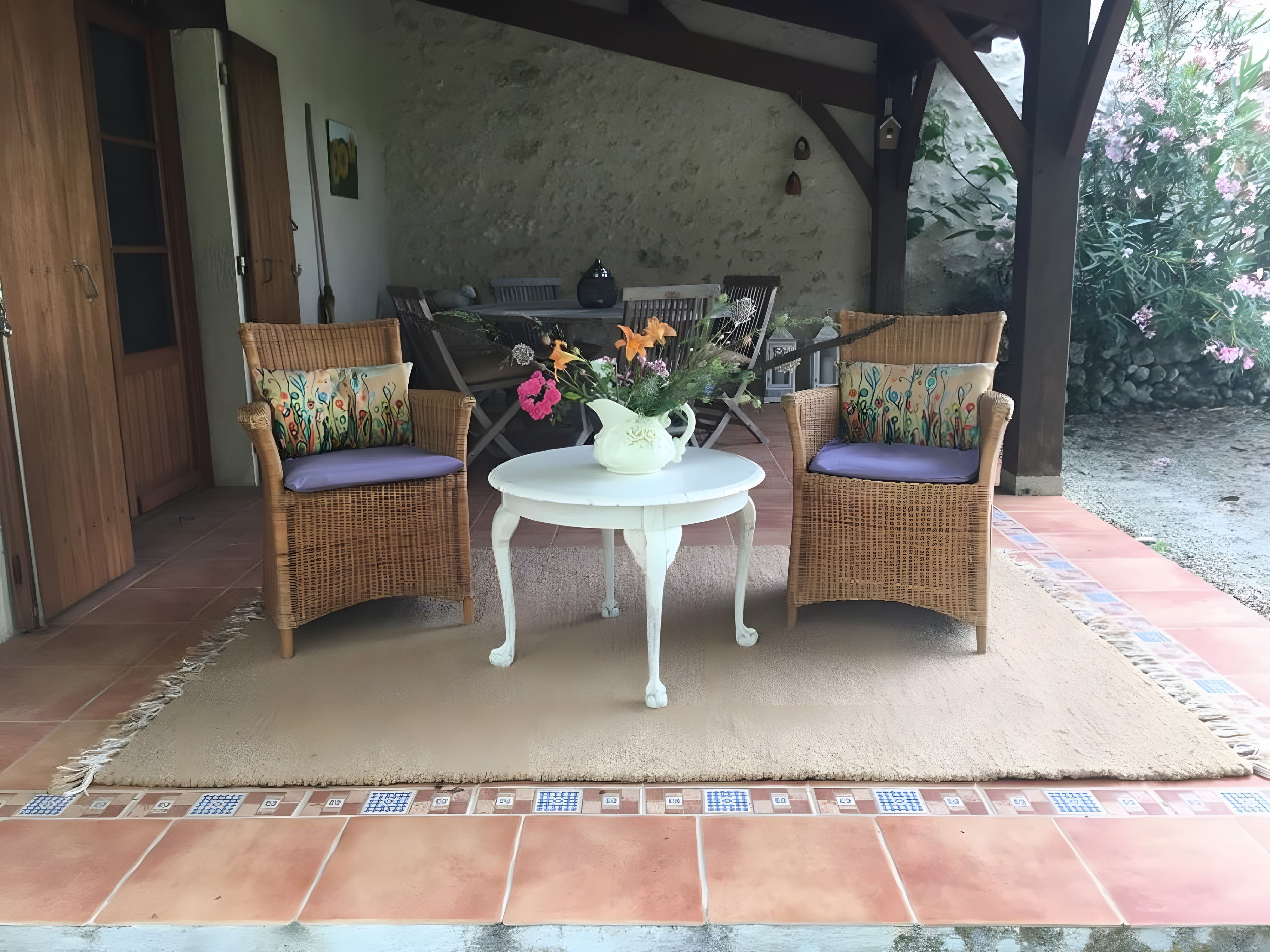 Un patio couvert comprenant deux fauteuils en osier, une petite table ronde et un vase rempli de fleurs.