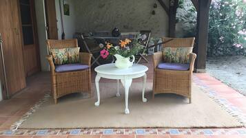 Un patio couvert comprenant deux fauteuils en osier, une petite table ronde et un vase rempli de fleurs.
