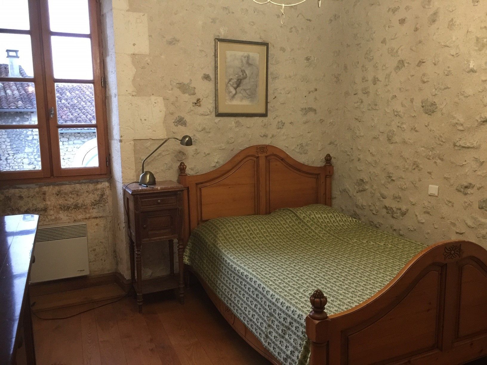 A bedroom with a wooden bed, a nightstand, a desk, and a window.
