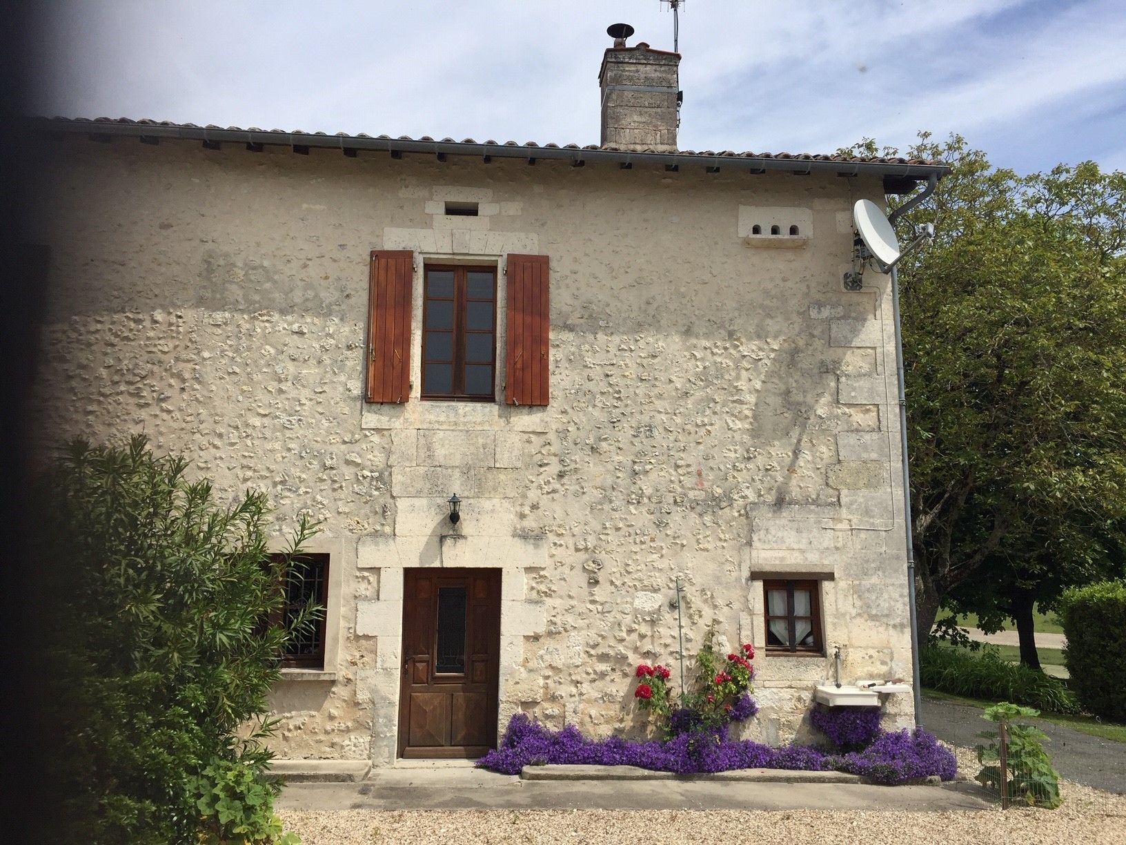 Un bâtiment en pierre avec une porte en bois, deux fenêtres avec volets et une antenne parabolique.