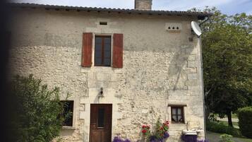 Un bâtiment en pierre avec une porte en bois, deux fenêtres avec volets et une antenne parabolique.