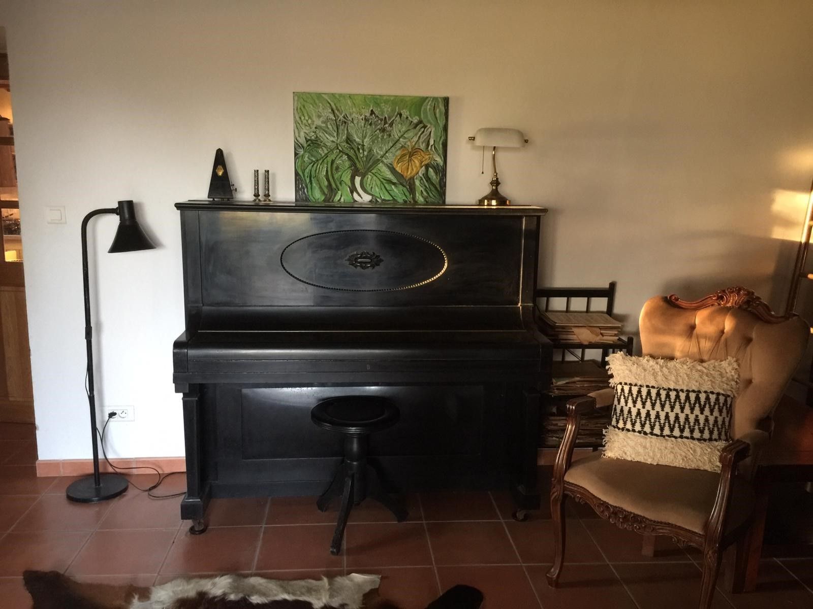 Une pièce avec un piano, une chaise dotée d’un coussin à motifs, un tableau accroché au mur et une lampe.