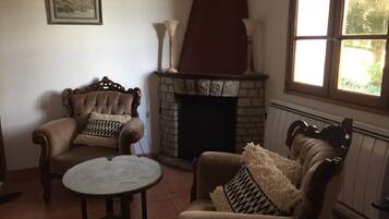 A cozy living room with a fireplace, two armchairs, a small round table, and a window with natural light.