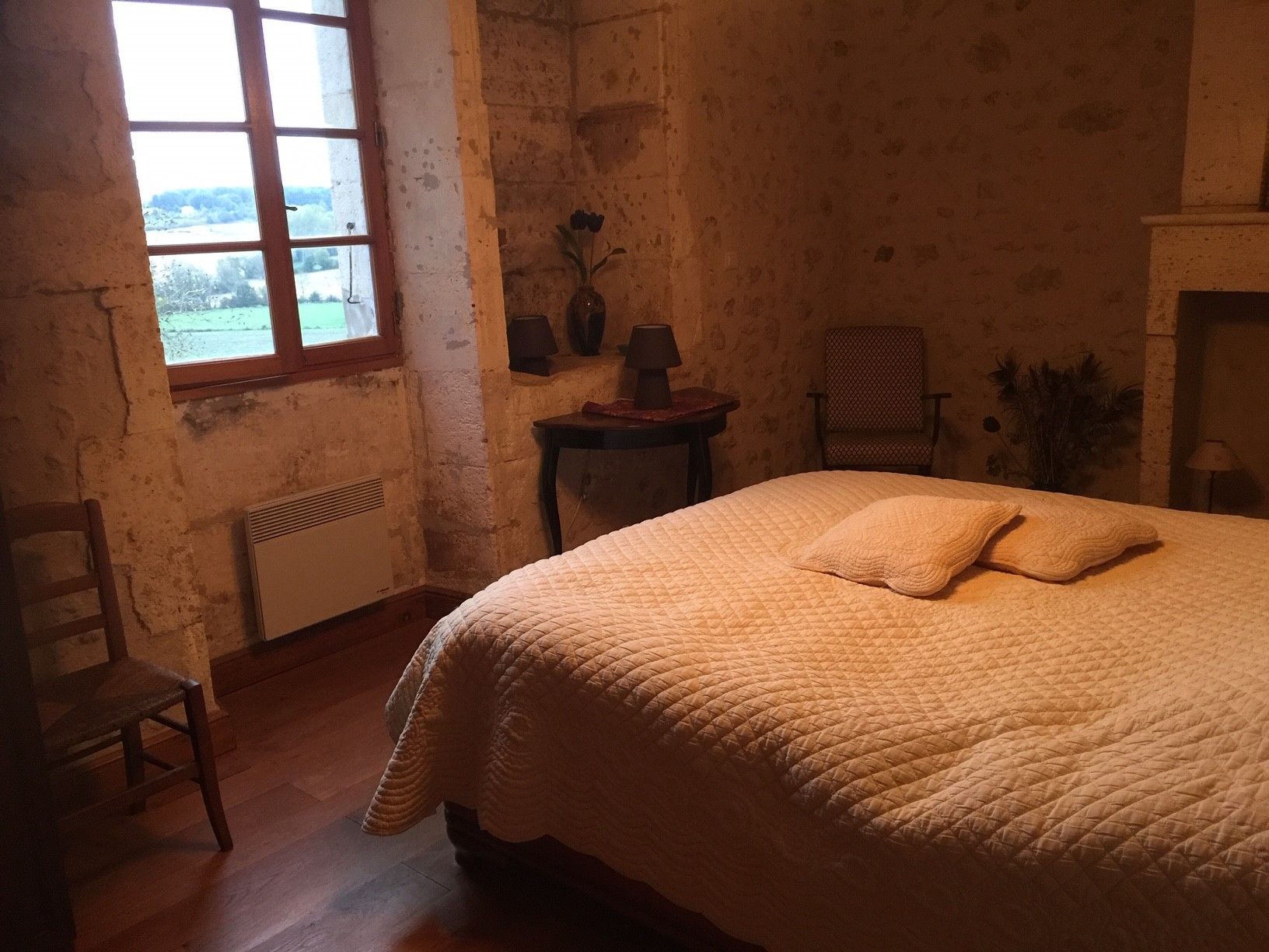 Een kamer met een bed, een stoel, een tafel met een lamp en een open haard.