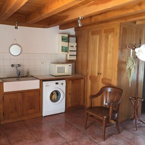 A compact kitchen with wooden cabinets, a washing machine, a microwave, and a chair. - Holiday Home 'Les Indeaux' with Private Pool, Private Terrace and Wi-Fi (Lusignac)
