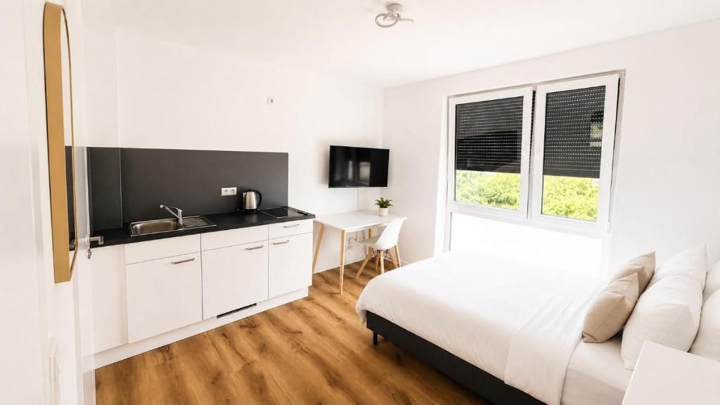 A modern bedroom with a large bed, a small desk, and a kitchenette area.