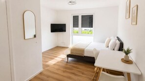Un dormitori modern amb un llit, una taula de nit i una televisió penjada a la paret.