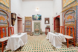 A room with two tables, chairs, a wall-mounted TV, a decorative door, and a patterned floor. - Dar fés (Fes)