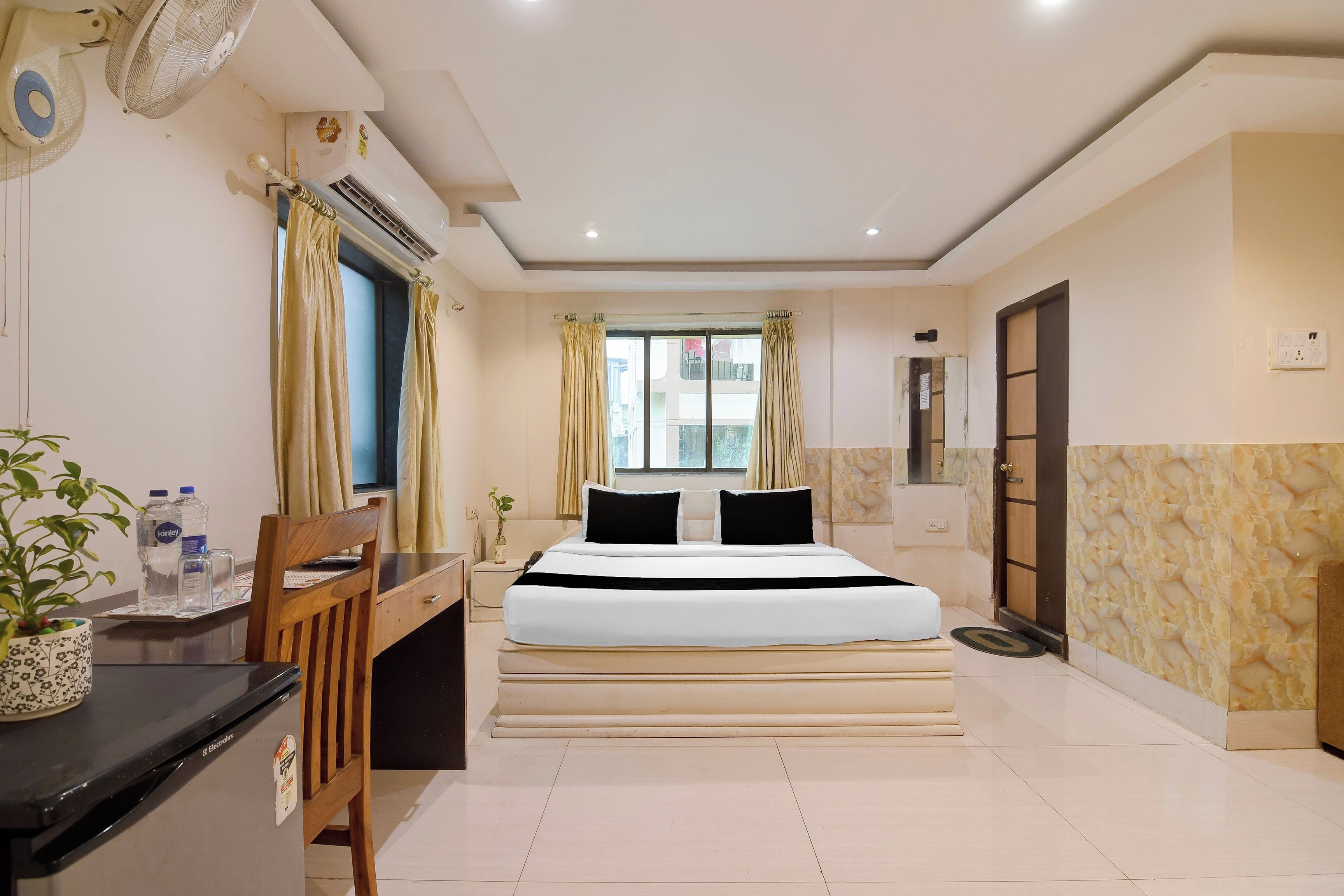 Habitación de hotel con una cama, un escritorio, una silla, una planta en maceta y una ventana con cortinas.